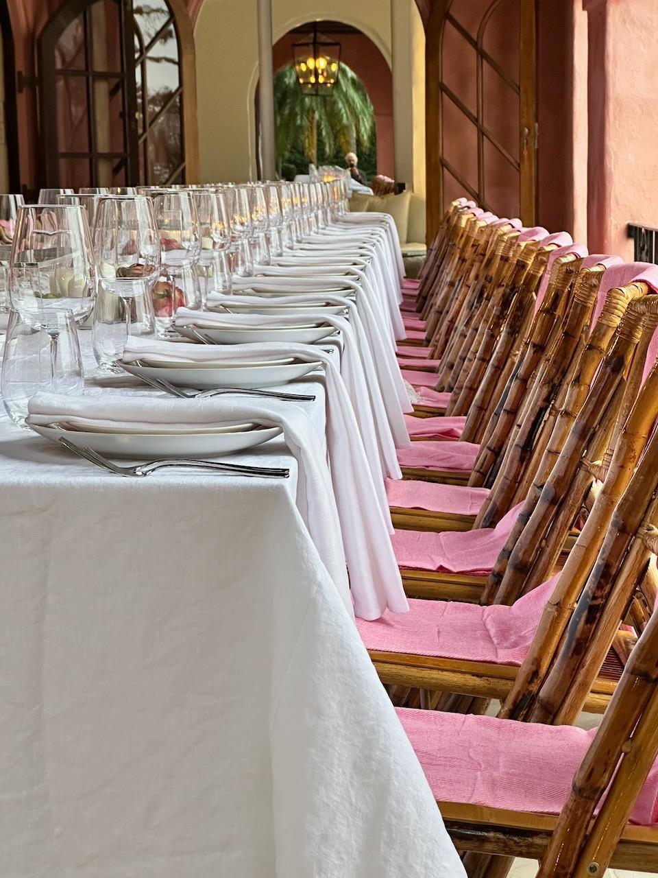 Bamboo chairs with pink cushions beside long white linen table in the loggia