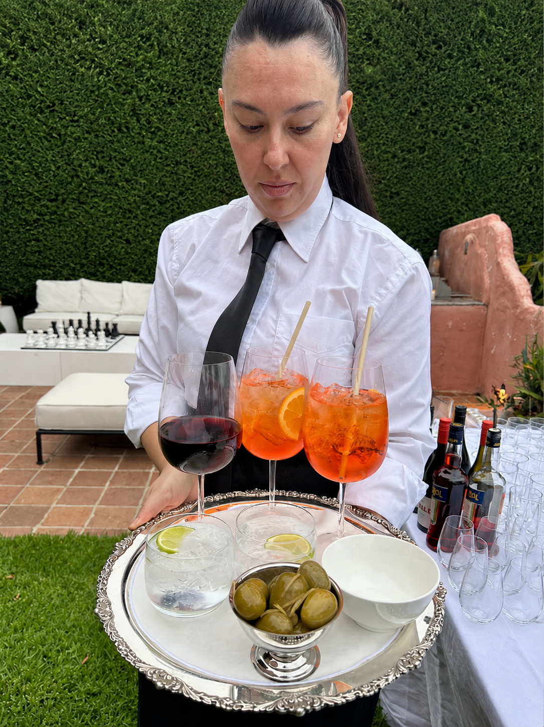Professional bartender presenting drinks on silver tray in garden setting