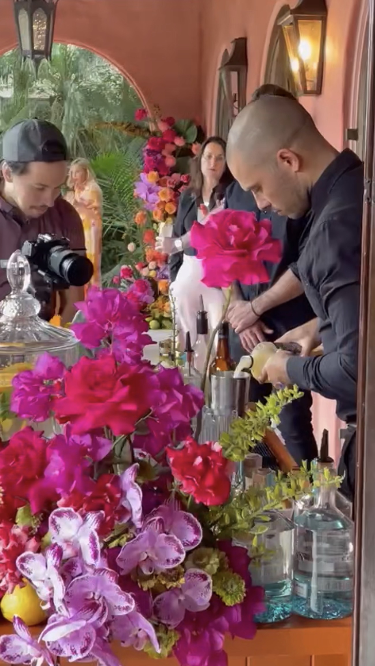 Bartender mixing cocktails at vivid floral bar with magenta roses and purple orchids in the terracotta loggia