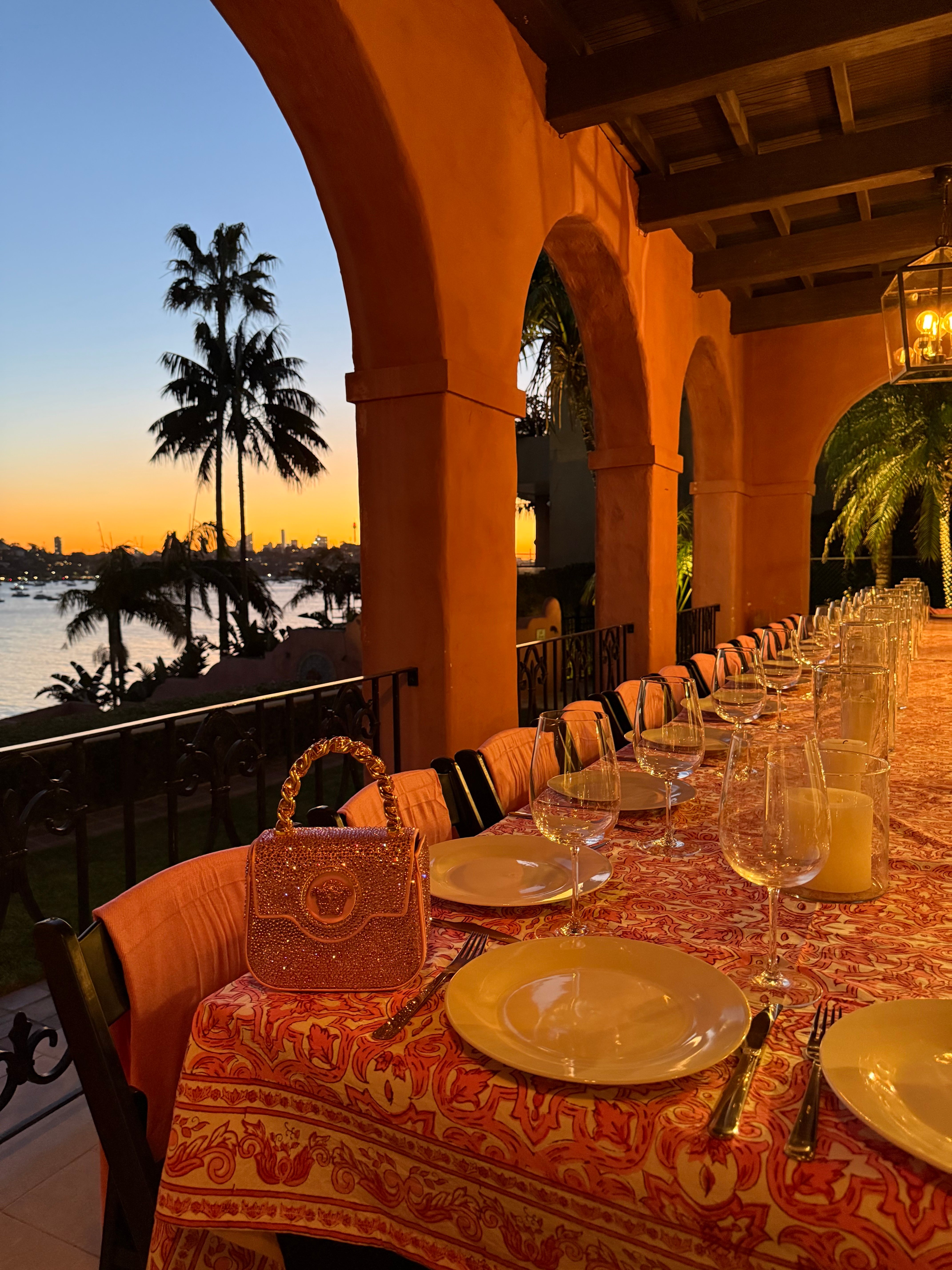 Loggia dinner with orange patterned tablecloth, pink arches and harbour sunset views