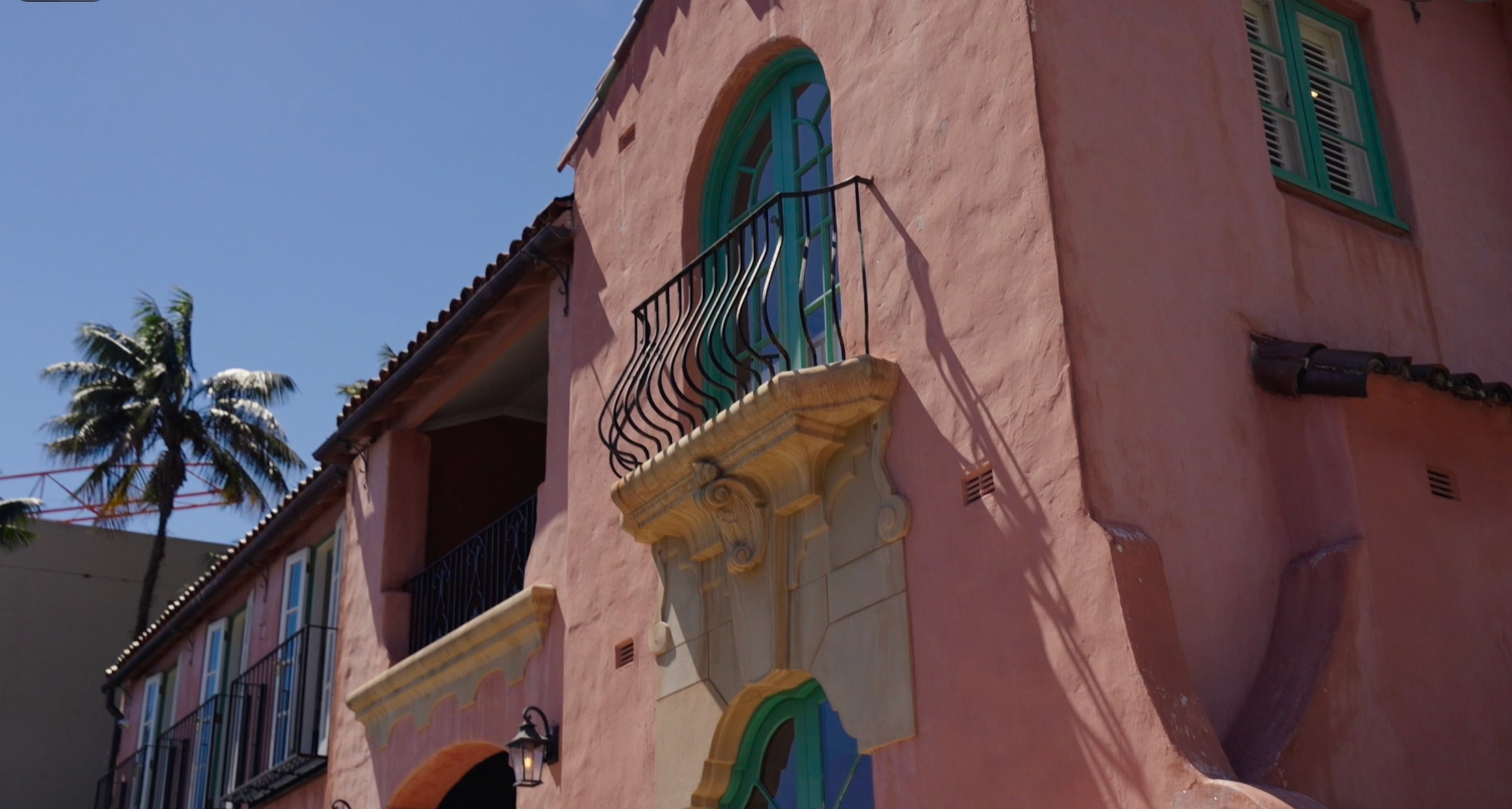 Pink facade with arched green-framed window, wrought iron Juliet balcony and carved sandstone corbel