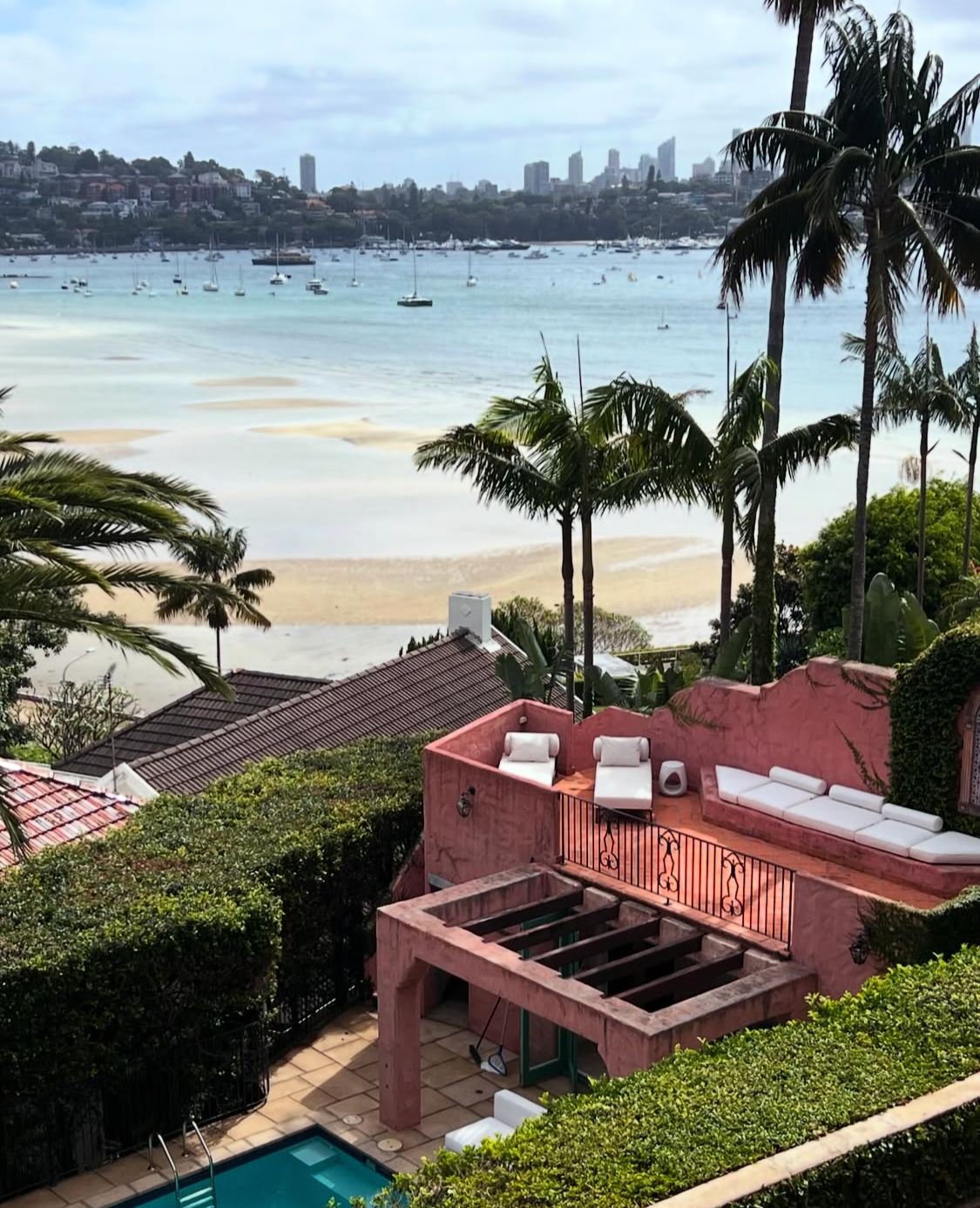 Rose Bay harbour with moored boats, Sydney CBD skyline and Villa Biscaya pool terrace with palm trees