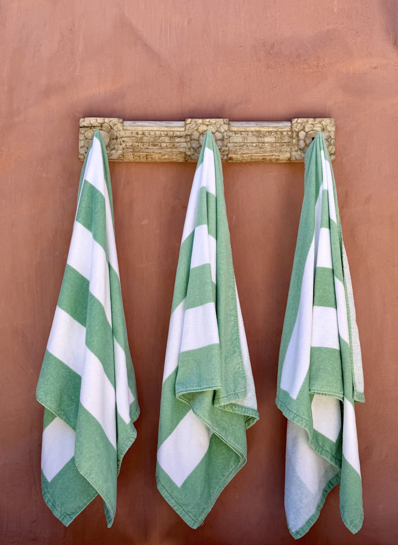 Green and white striped beach towels on carved wooden rack