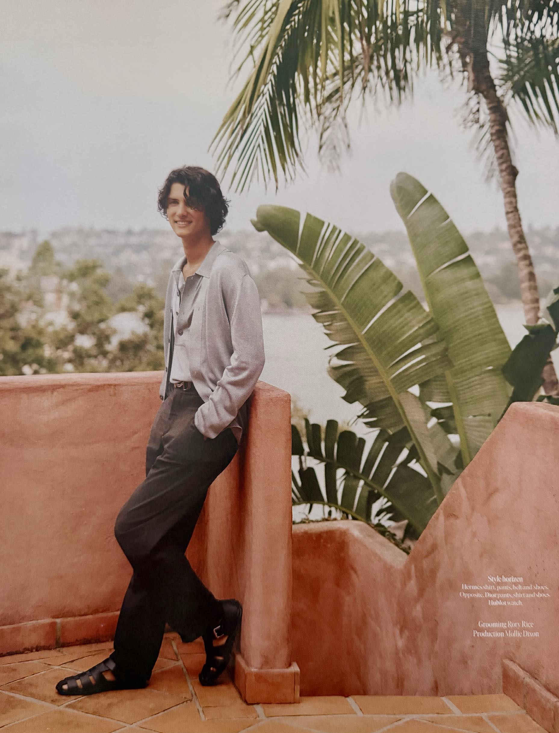 Count Nikolai in Hermes on rooftop terrace with palm trees and harbour views